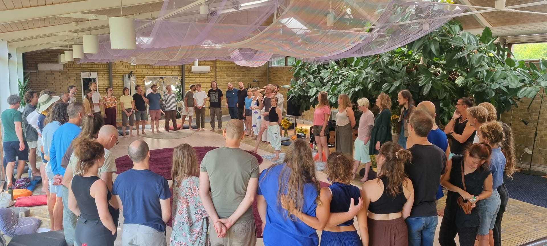 A large circle of participants standing arm in arm in the Pool Room at Nära Summer Festival 2026