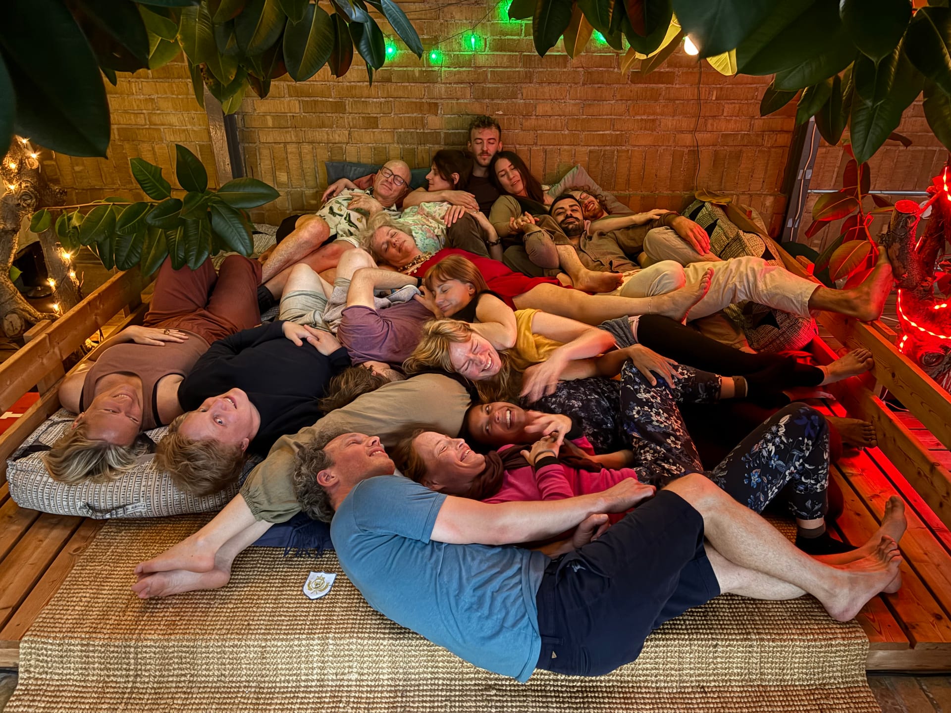 A group of participants resting together in a cosy pile of bodies under warm red light
