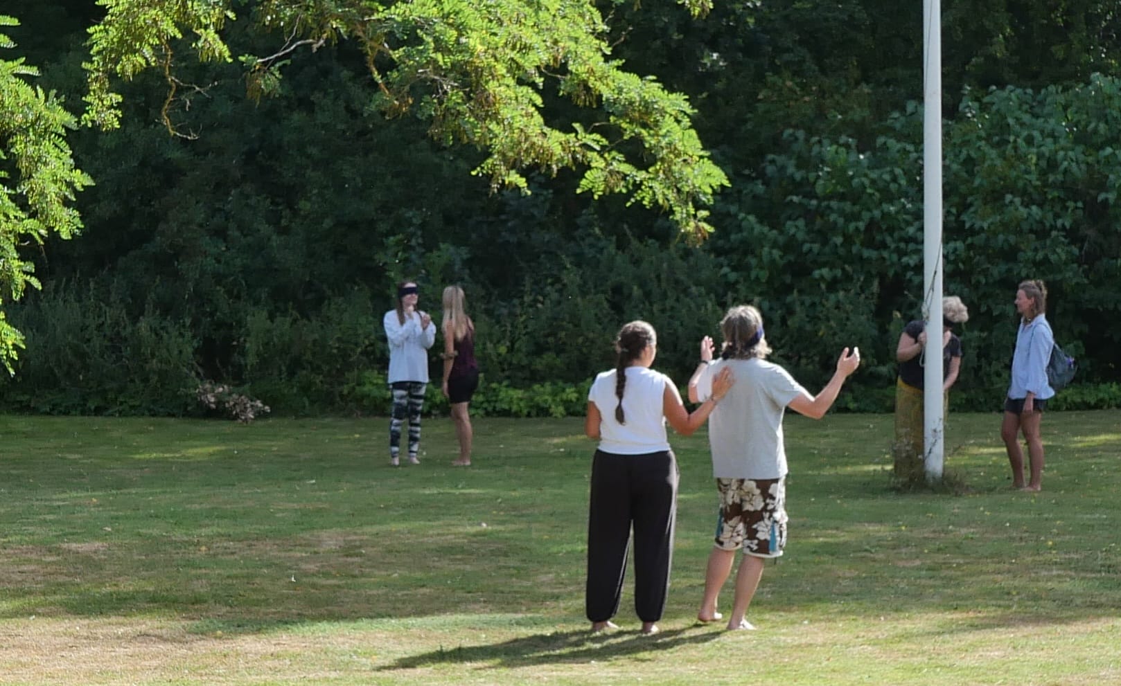 Pairs of participants doing a partner exercise on the lawn by the flagpole