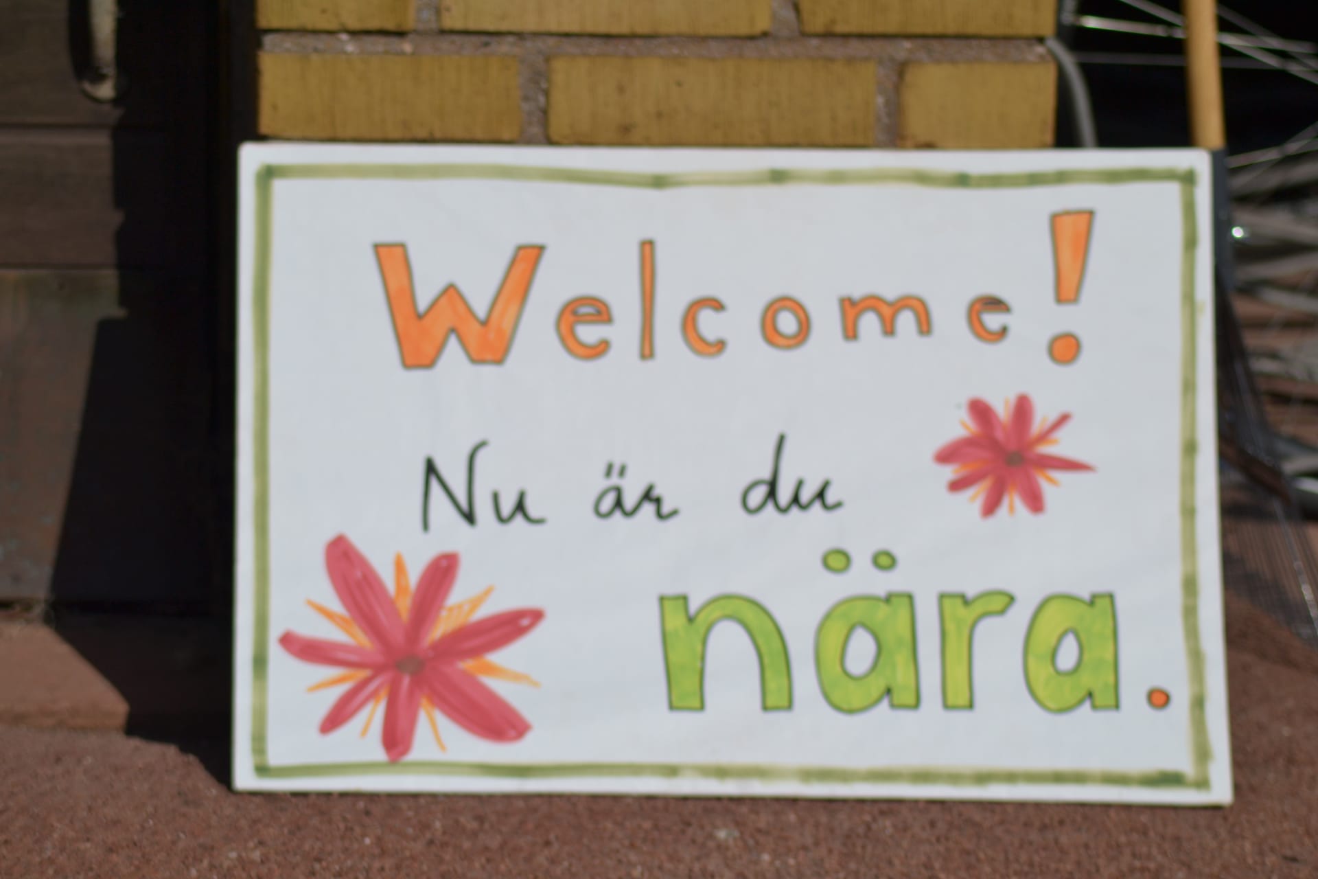 Hand-painted sign with flowers reading Welcome! Nu är du nära.